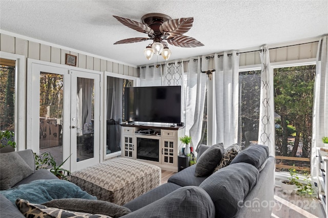 living room with wooden walls, a wealth of natural light, ceiling fan, and a textured ceiling