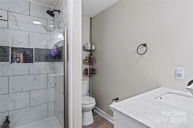 bathroom with a tile shower, vanity, a textured ceiling, hardwood / wood-style floors, and toilet