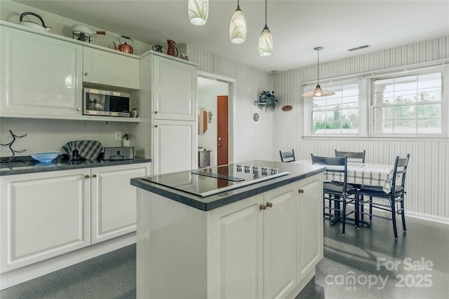 kitchen featuring white cabinetry, stainless steel microwave, hanging light fixtures, and dark countertops