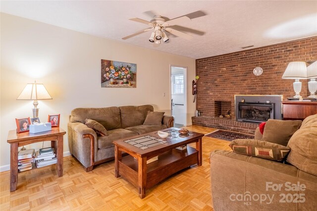 living room featuring baseboards, a brick fireplace, a textured ceiling, and a ceiling fan