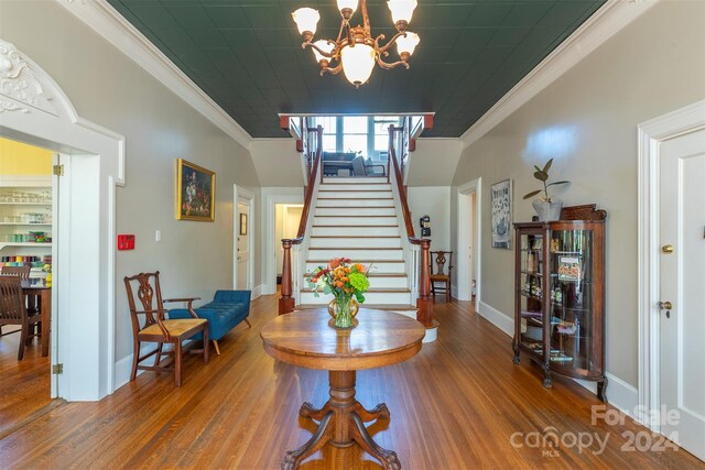 foyer with wood-type flooring, an inviting chandelier, and crown molding