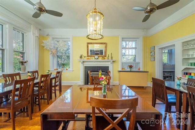 dining space featuring a tiled fireplace, wood-type flooring, and ceiling fan with notable chandelier