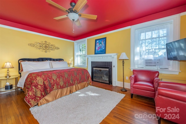 bedroom featuring a tiled fireplace, ceiling fan, and hardwood / wood-style floors