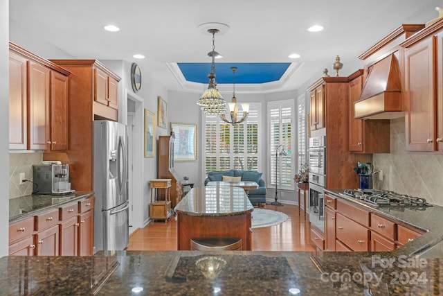 kitchen with hanging light fixtures, premium range hood, appliances with stainless steel finishes, and light hardwood / wood-style flooring