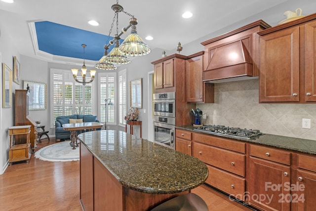 kitchen with light wood-type flooring, stainless steel appliances, decorative light fixtures, and custom exhaust hood