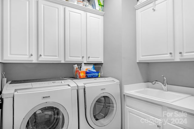 clothes washing area with cabinets, washing machine and dryer, and sink