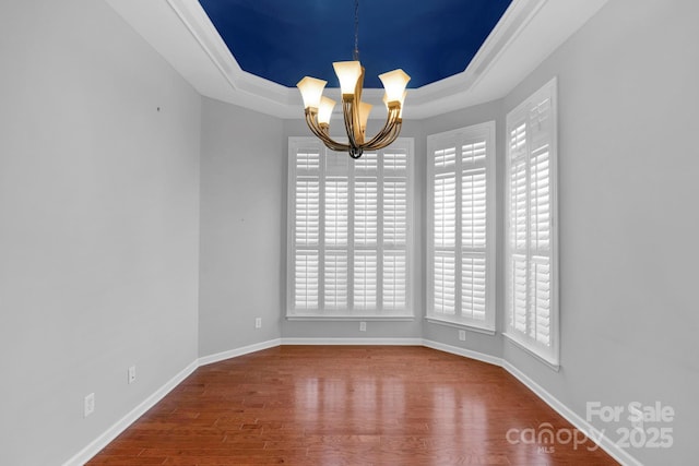 unfurnished dining area with wood finished floors, baseboards, ornamental molding, a tray ceiling, and an inviting chandelier