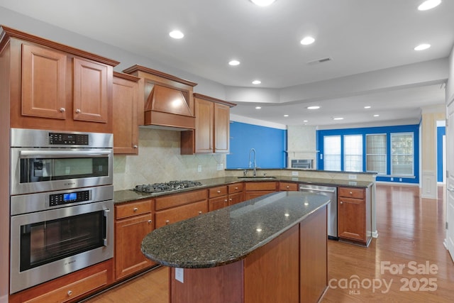 kitchen featuring visible vents, a peninsula, custom exhaust hood, stainless steel appliances, and a sink