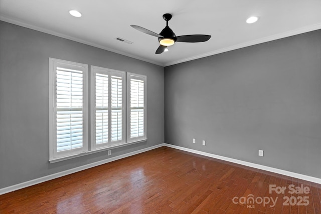 empty room with baseboards, crown molding, visible vents, and wood finished floors