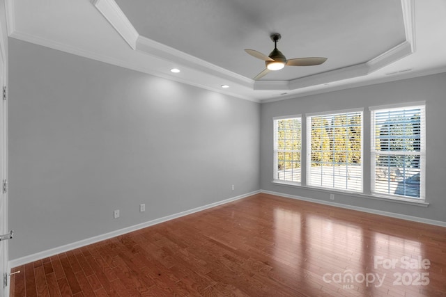 empty room featuring a raised ceiling, crown molding, baseboards, and wood finished floors