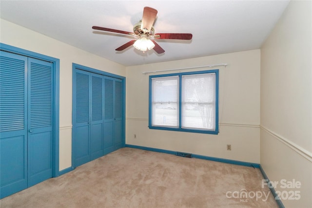 unfurnished bedroom featuring ceiling fan, light colored carpet, and multiple closets