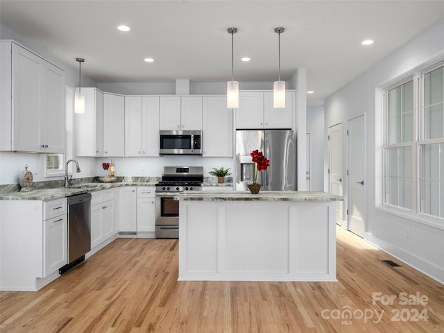 kitchen with white cabinetry, stainless steel appliances, decorative light fixtures, and light hardwood / wood-style flooring