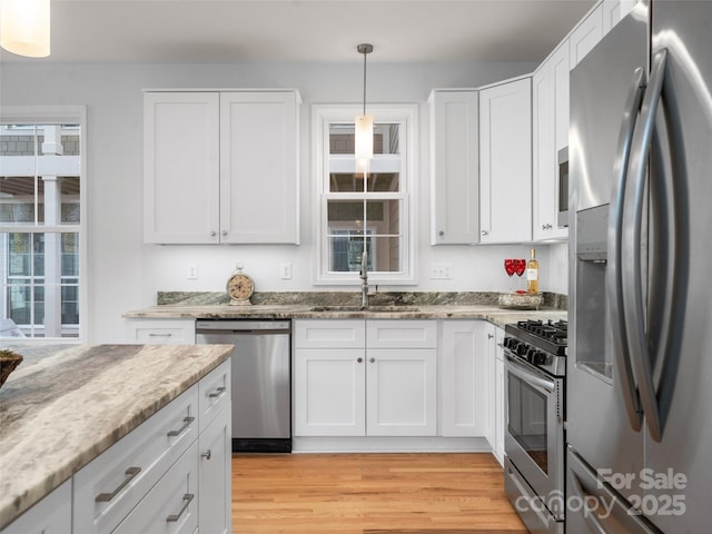 kitchen with a sink, white cabinetry, light stone countertops, appliances with stainless steel finishes, and light wood-style floors
