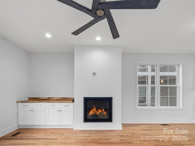unfurnished living room with light wood-type flooring, visible vents, and a glass covered fireplace