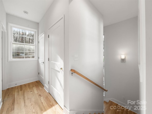 corridor with baseboards, an upstairs landing, and light wood-style floors