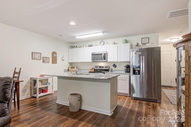 kitchen with white cabinets, dark hardwood / wood-style floors, an island with sink, and appliances with stainless steel finishes