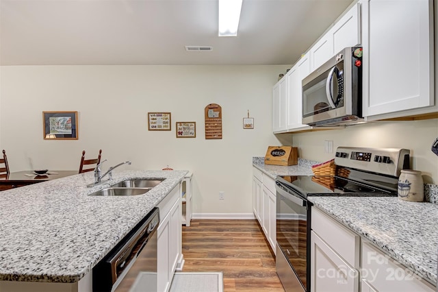 kitchen with stainless steel appliances, white cabinets, sink, light stone countertops, and light wood-type flooring