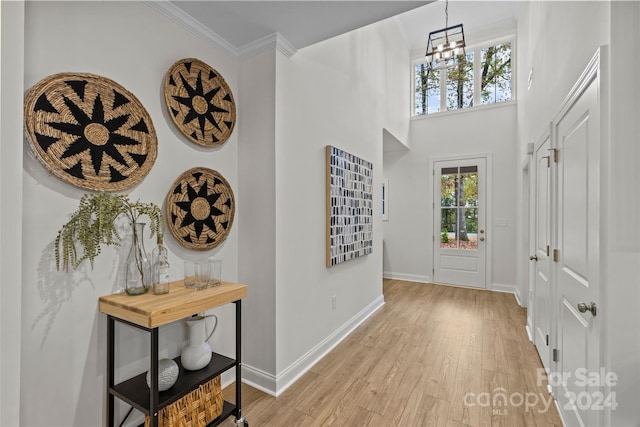 entryway with ornamental molding, light wood-type flooring, a chandelier, and a high ceiling