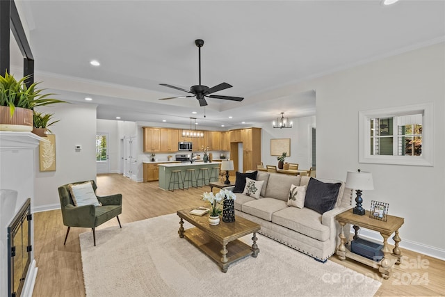 living room with ceiling fan with notable chandelier, light wood-type flooring, and ornamental molding