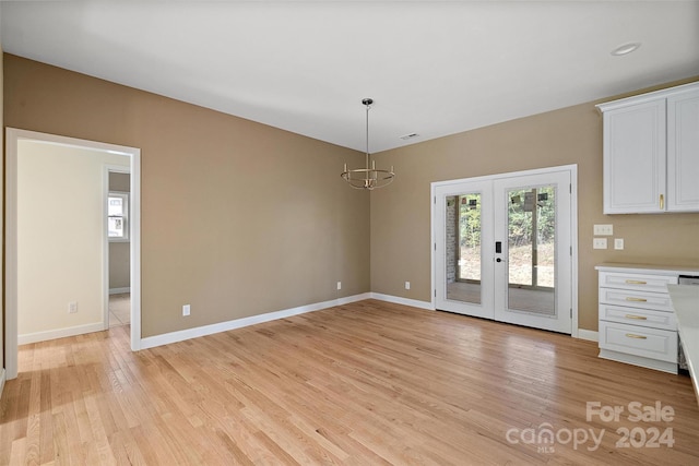 unfurnished dining area featuring light hardwood / wood-style floors, a chandelier, and french doors