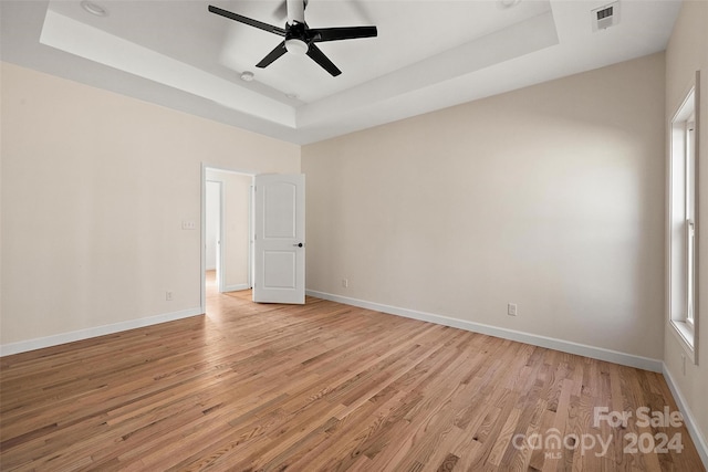 unfurnished room with a healthy amount of sunlight, light hardwood / wood-style flooring, ceiling fan, and a tray ceiling