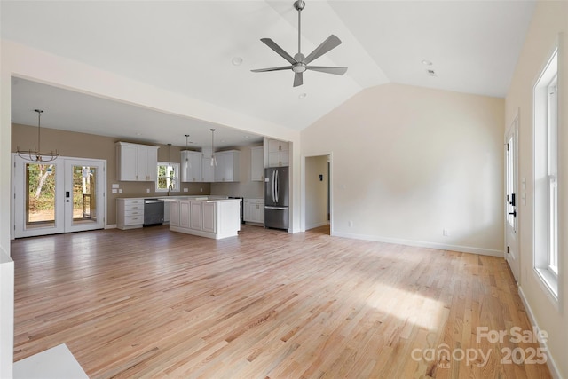 unfurnished living room with ceiling fan with notable chandelier, vaulted ceiling, and light hardwood / wood-style flooring