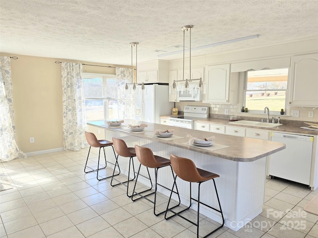 kitchen with white appliances, a kitchen island, pendant lighting, white cabinets, and sink