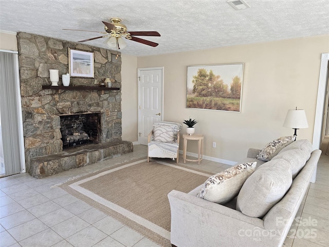 tiled living room featuring ceiling fan, a textured ceiling, and a stone fireplace