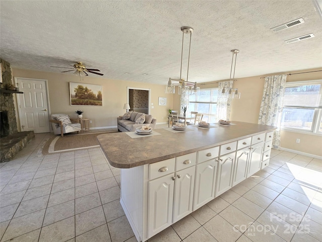 kitchen with white cabinetry, decorative light fixtures, light tile patterned flooring, a kitchen island, and ceiling fan with notable chandelier