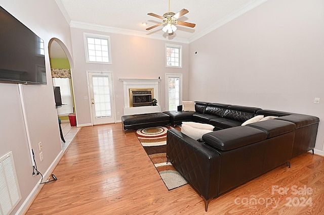 living room with ceiling fan, light wood-type flooring, ornamental molding, and a towering ceiling