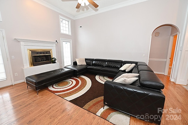 living room with ceiling fan, crown molding, a high ceiling, and light hardwood / wood-style flooring