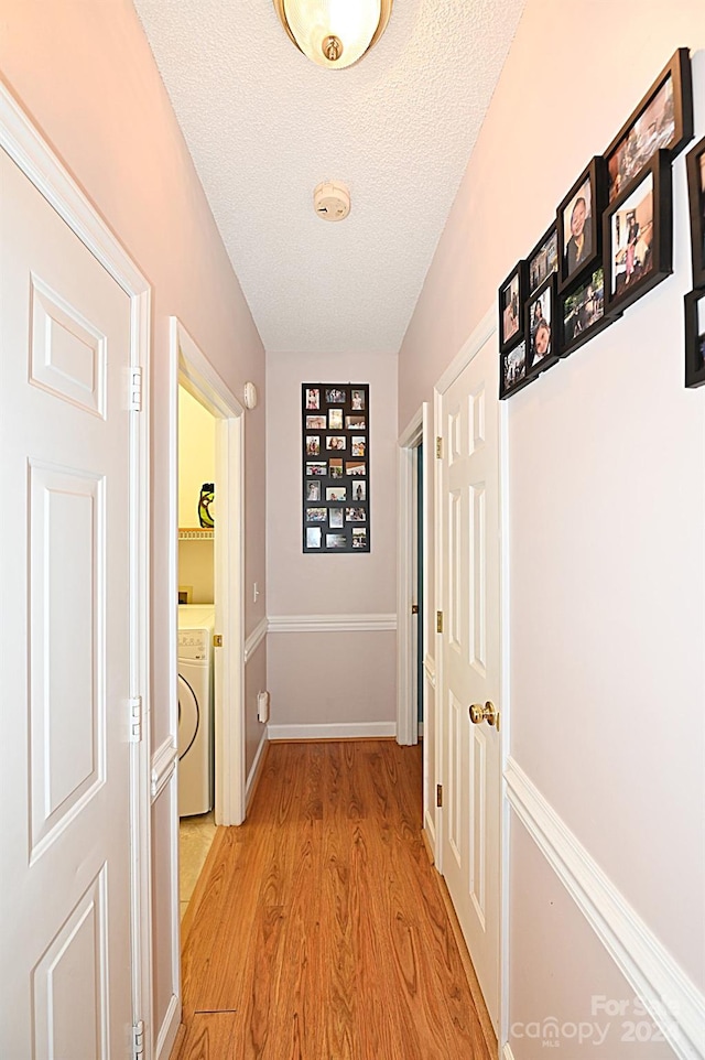 corridor featuring light hardwood / wood-style floors, a textured ceiling, and washer / dryer