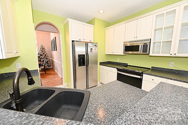 kitchen featuring appliances with stainless steel finishes, light wood-type flooring, a textured ceiling, sink, and white cabinets