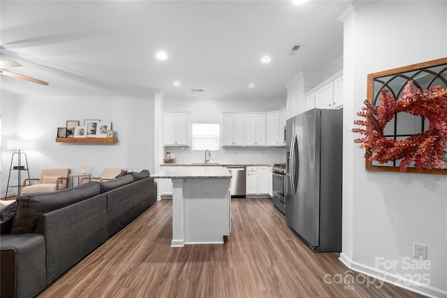 kitchen featuring stainless steel appliances, white cabinetry, tasteful backsplash, light stone countertops, and a kitchen island