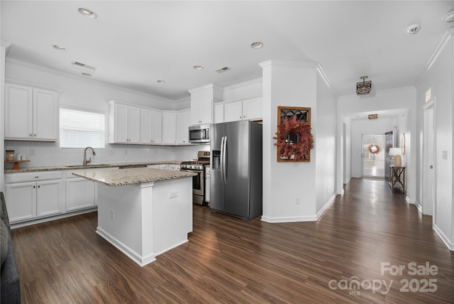 kitchen featuring appliances with stainless steel finishes, sink, a kitchen island, white cabinets, and tasteful backsplash