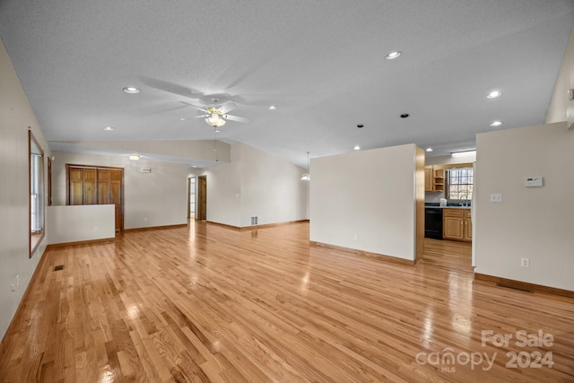 unfurnished living room featuring ceiling fan, sink, light hardwood / wood-style floors, a textured ceiling, and lofted ceiling