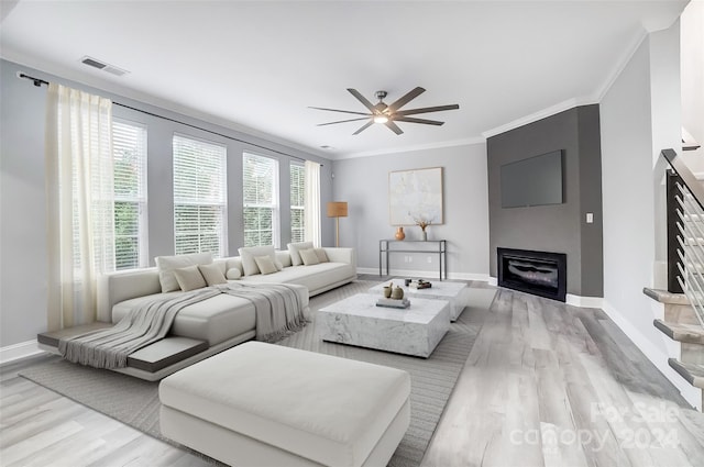 living room with a large fireplace, light hardwood / wood-style flooring, ceiling fan, and crown molding