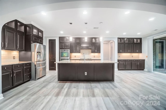 kitchen featuring stainless steel appliances, backsplash, pendant lighting, dark brown cabinets, and a center island with sink