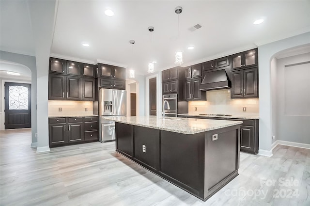 kitchen with a kitchen island with sink, decorative light fixtures, decorative backsplash, custom range hood, and appliances with stainless steel finishes