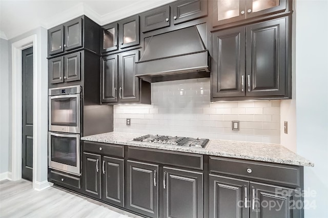 kitchen with decorative backsplash, light wood-type flooring, light stone counters, custom exhaust hood, and stainless steel appliances