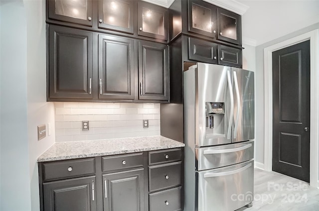 kitchen with stainless steel refrigerator with ice dispenser, tasteful backsplash, light stone counters, dark brown cabinets, and crown molding