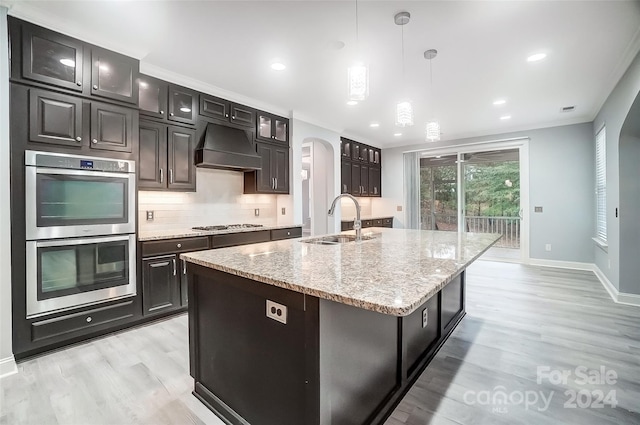 kitchen with sink, stainless steel appliances, pendant lighting, a center island with sink, and custom exhaust hood