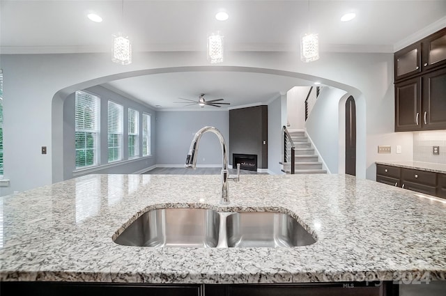 kitchen featuring a center island with sink, light stone countertops, sink, and hanging light fixtures