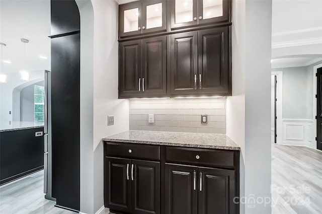 bar featuring tasteful backsplash, light stone countertops, light hardwood / wood-style flooring, and dark brown cabinets