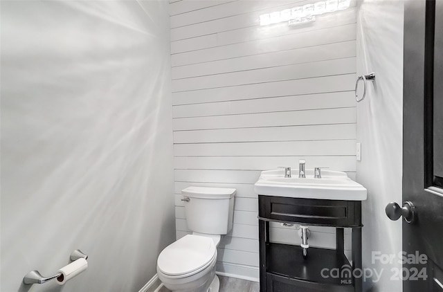 bathroom featuring toilet, wood-type flooring, sink, and wooden walls