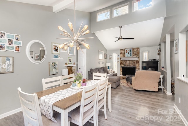 dining area featuring light wood finished floors, baseboards, beam ceiling, a stone fireplace, and high vaulted ceiling