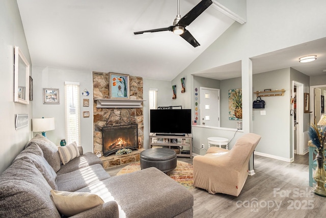 living area featuring vaulted ceiling with beams, baseboards, a fireplace, wood finished floors, and a ceiling fan