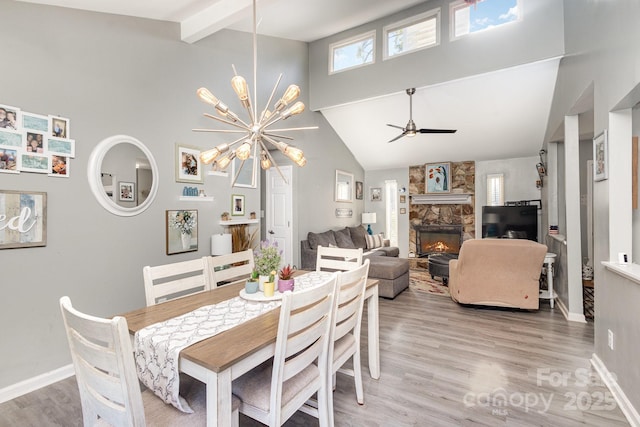 dining room with baseboards, light wood-type flooring, beam ceiling, a fireplace, and high vaulted ceiling