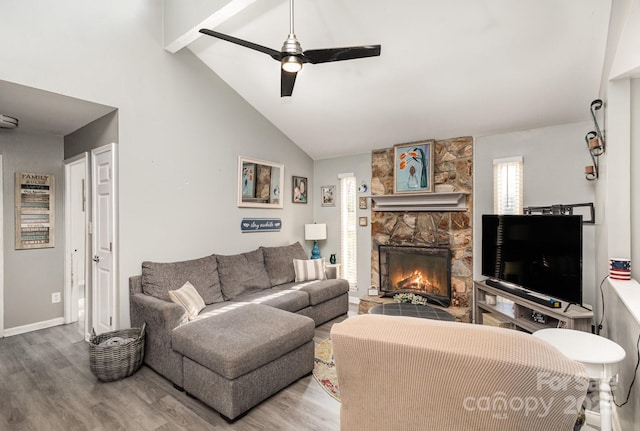 living area with baseboards, beamed ceiling, a fireplace, wood finished floors, and a ceiling fan