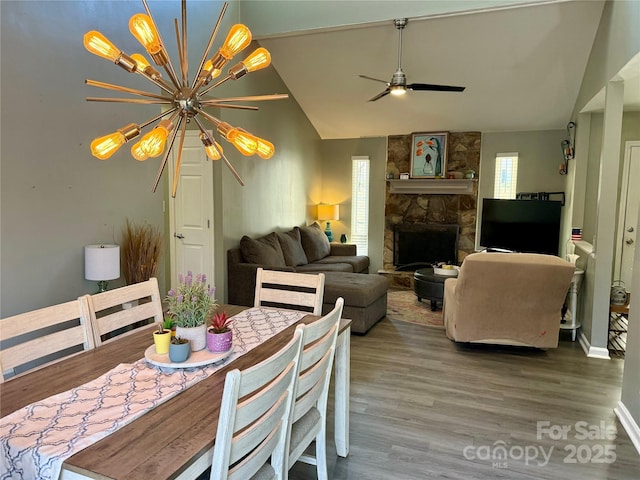 dining room with vaulted ceiling, a stone fireplace, a ceiling fan, and wood finished floors